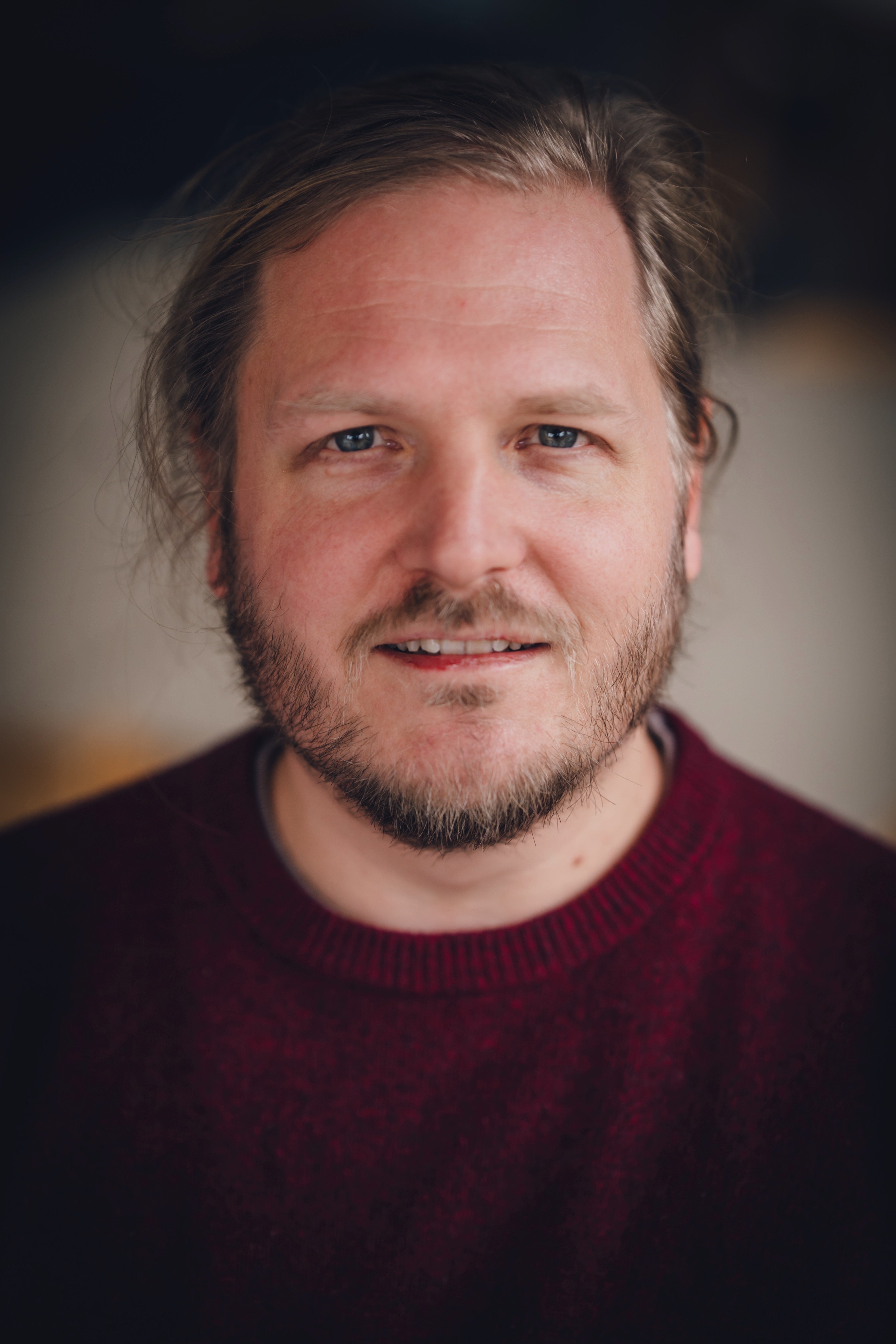 Portraitfoto eines mittelalten Mannes mit blonden Haaren und Bart in einem roten Pullover